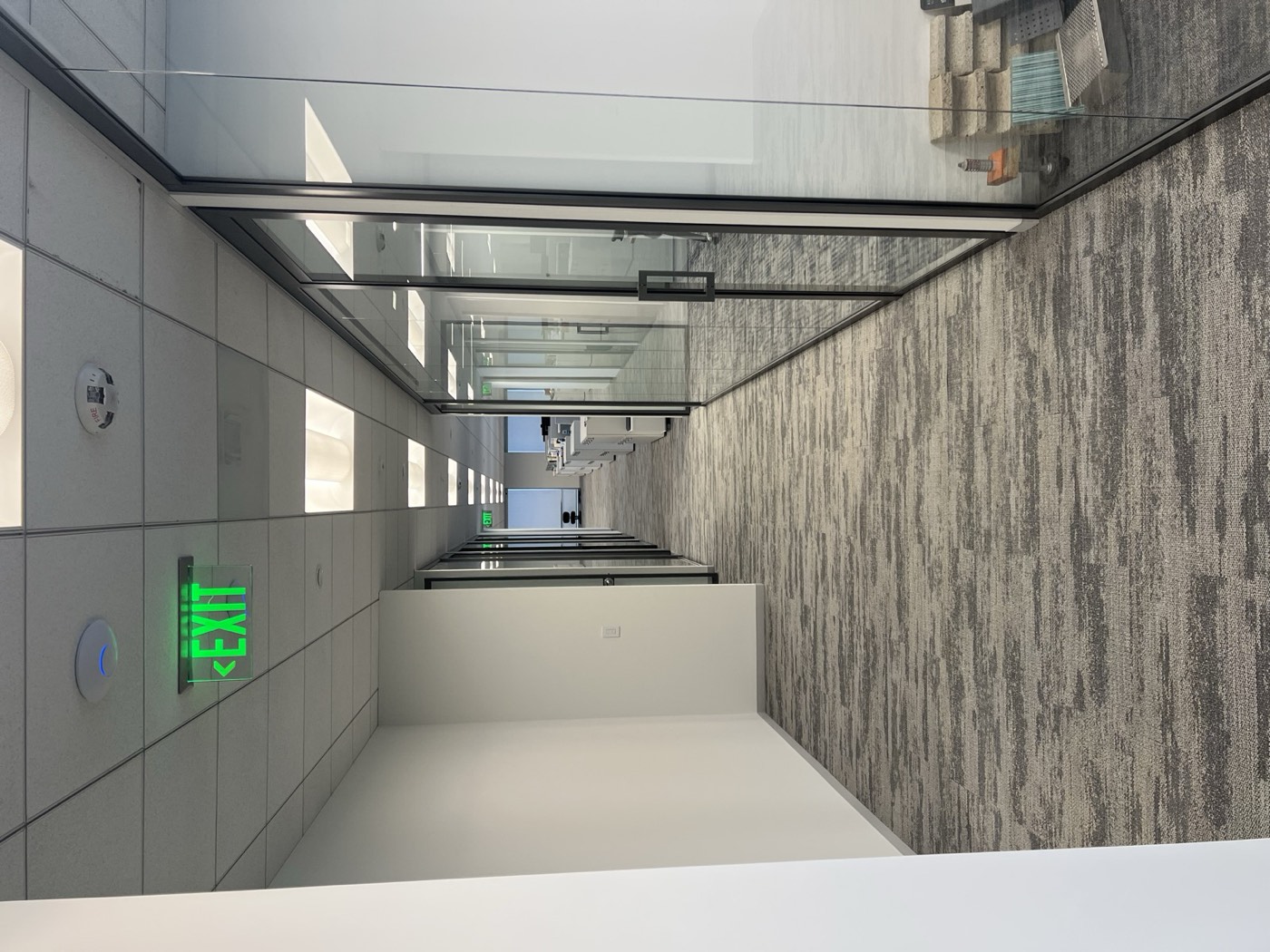 Glass-front office suites along a finished corridor with lit exit signage, Greenberg Farrow office tenant improvement